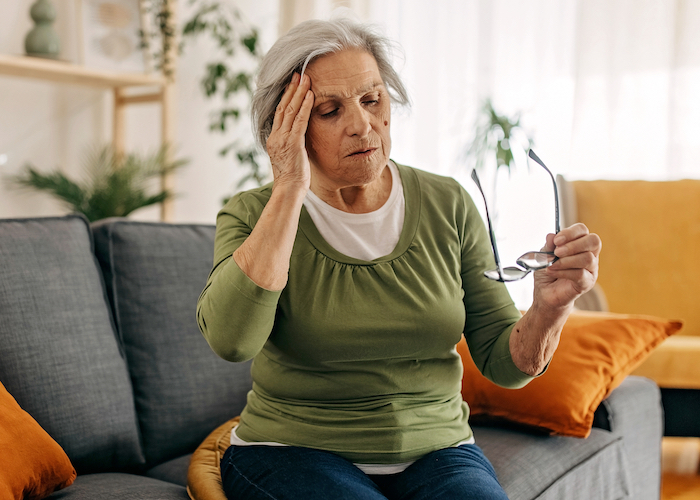 An older women sitting on her couch holding her head