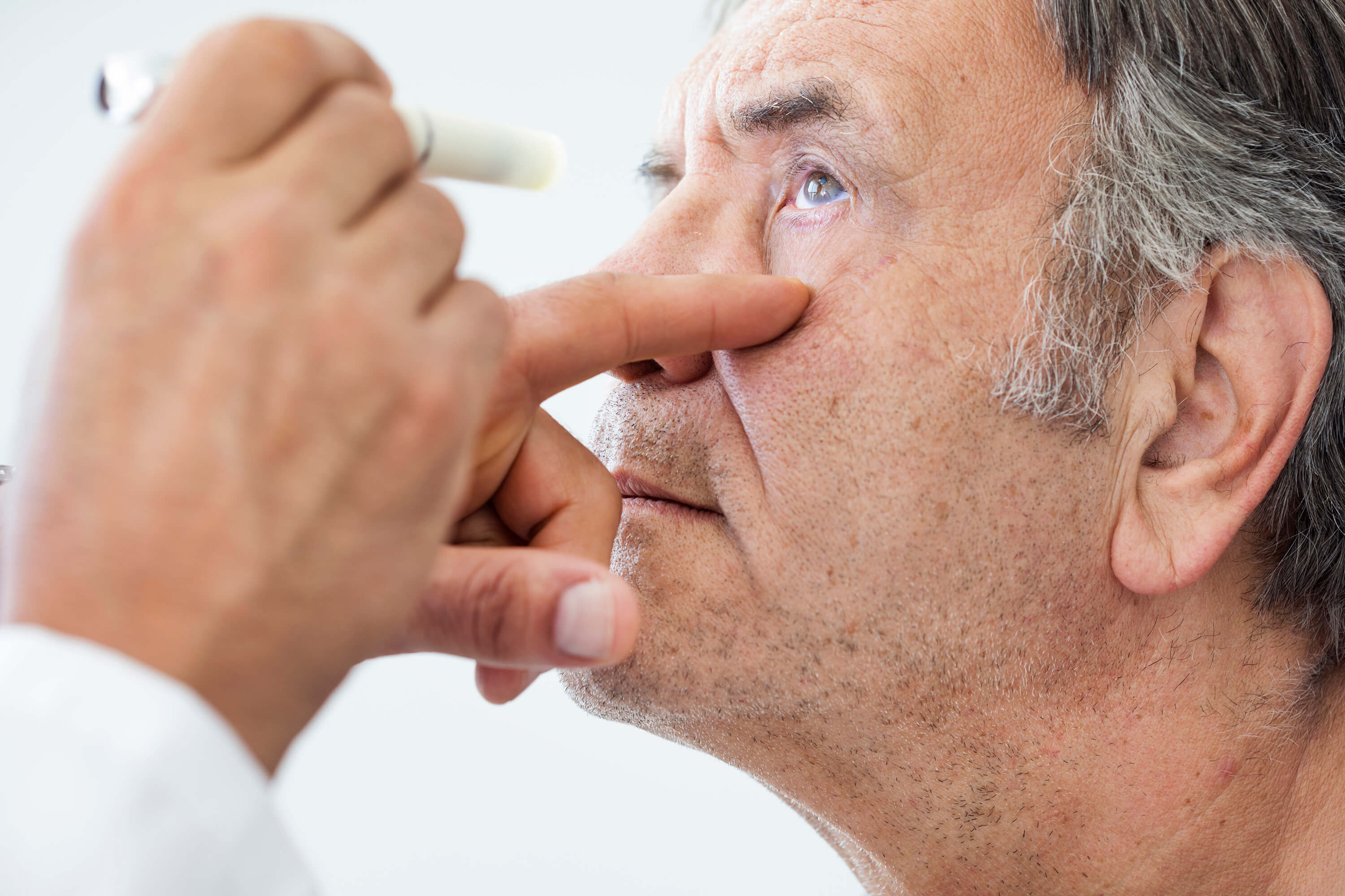 Doctor flashing a light in an older man's eye during an eye exam